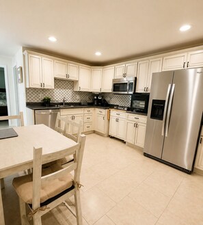 A modern kitchen with white cabinetry, stainless steel appliances, and a dining area with a wooden table and chairs.