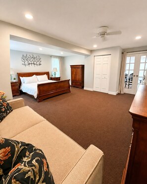 A spacious bedroom with a large bed, a wardrobe, a ceiling fan, and a view through a door.