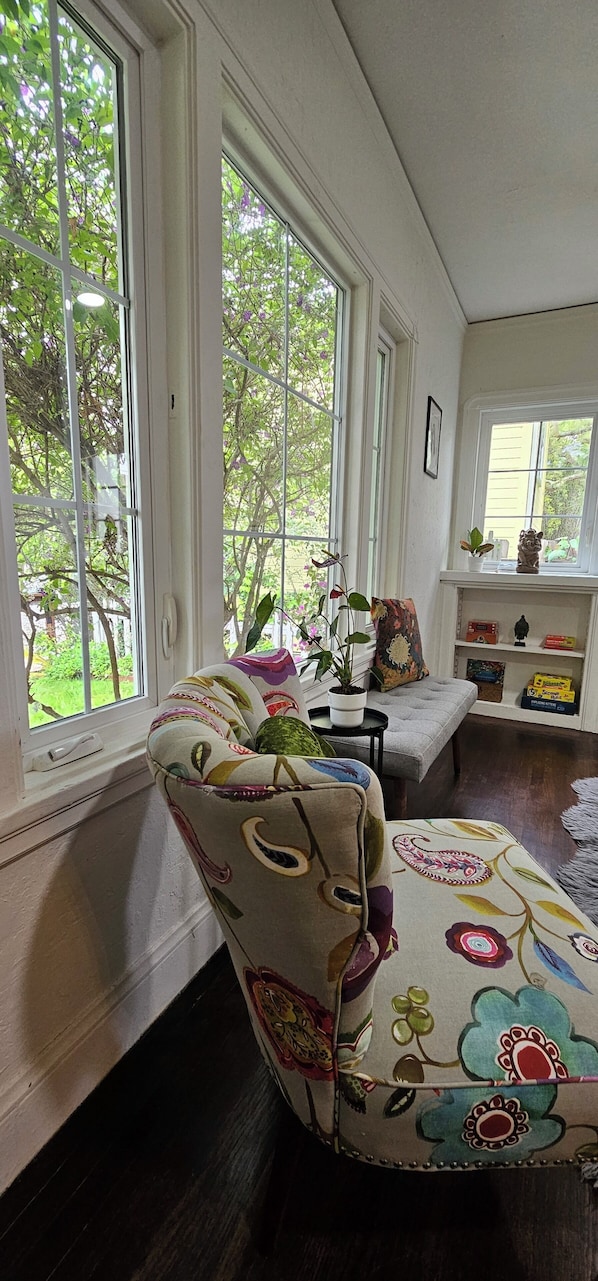 Una habitación con ventanas amplias, un banco acolchado, una planta en maceta y un estante con objetos.