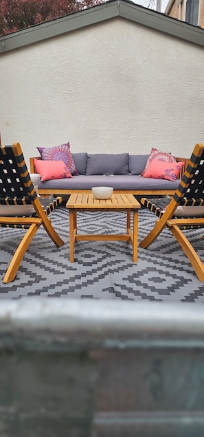 A sofa with patterned cushions, two wooden chairs, and a small table.
