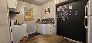 A compact kitchen with a gas stove, a refrigerator, and a dining table. - Charming 1920s Westbrae Berkeley Cottage with Soaking Tub! Walk to BART & Parks (Berkeley)