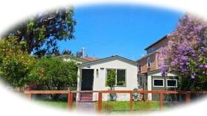 A residential building with a small porch, a garage, and a garden with flowering trees. - Charming 1920s Westbrae Berkeley Cottage with Soaking Tub! Walk to BART & Parks (Berkeley)