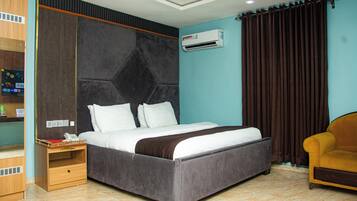 A hotel room with a bed, a nightstand, an air conditioner, a sofa, and a wall-mounted shelf.
