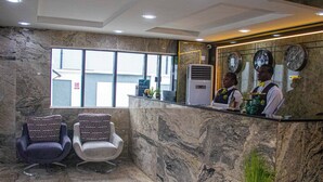 Un área de recepción con paredes de mármol, un mostrador de recepción, dos sillones y un ventanal grande.
