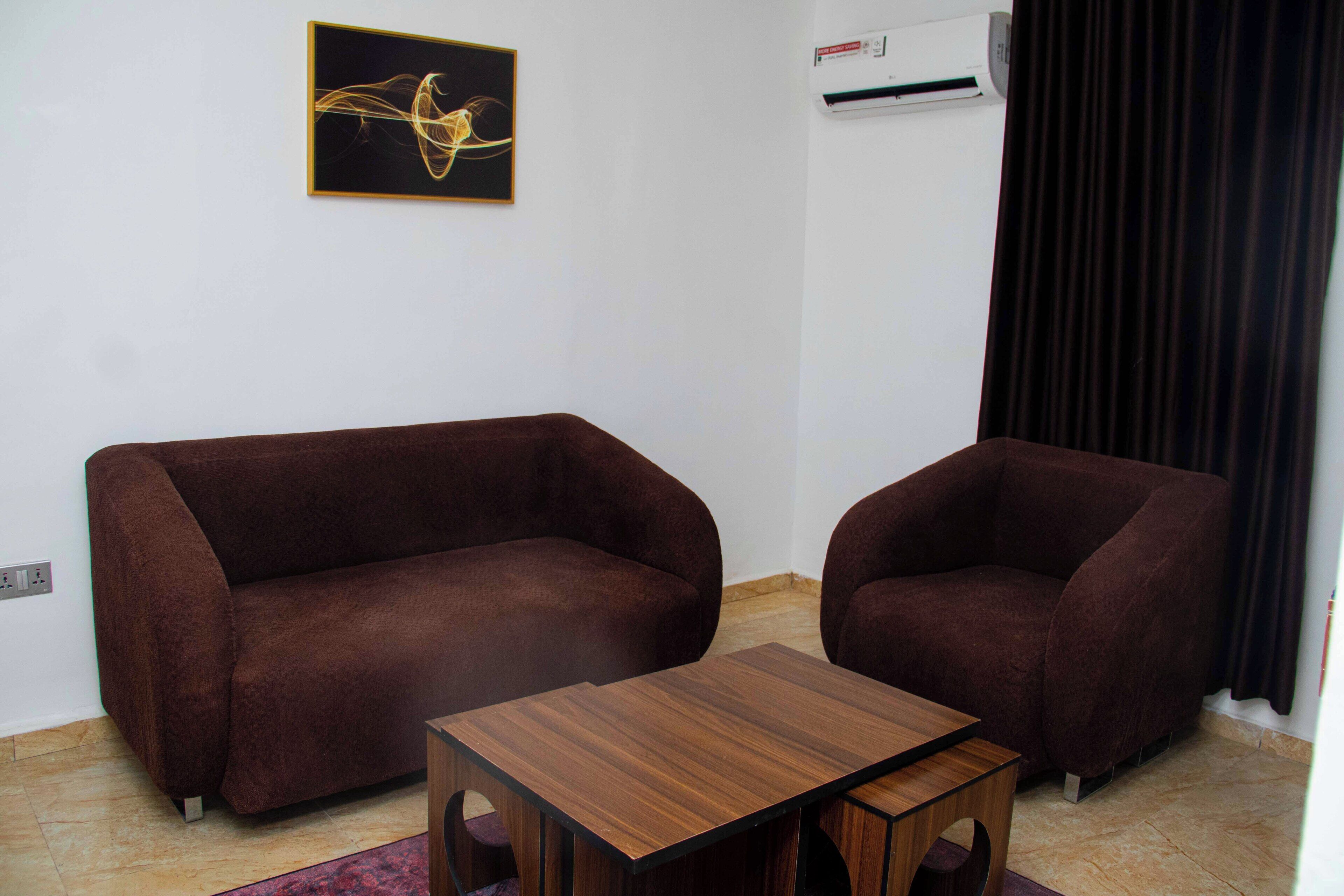 A room with two brown sofas, a wooden coffee table, a wall-mounted air conditioner, and a framed abstract painting.
