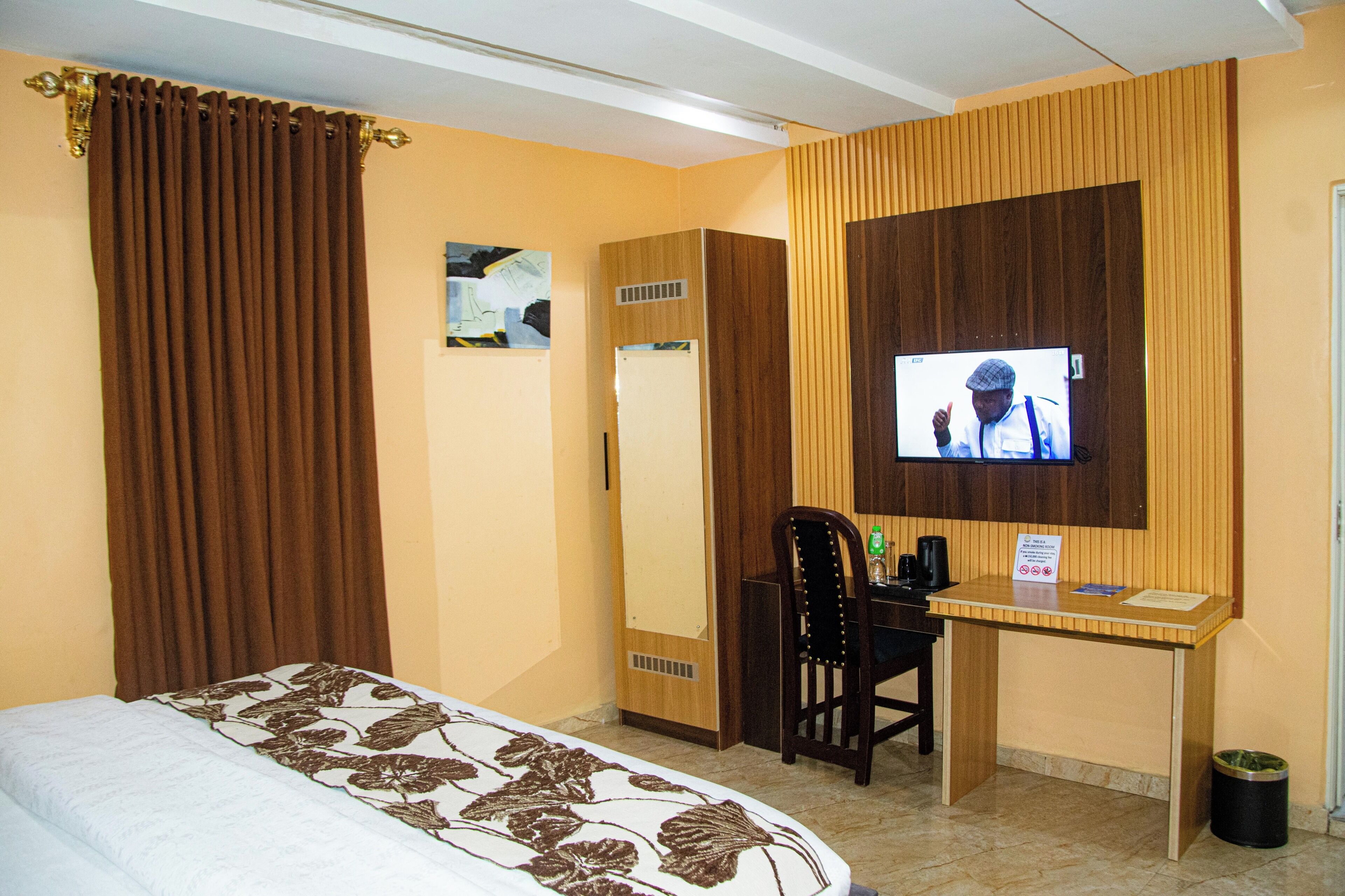 Una camera d'albergo con un letto, una scrivania, una televisione, un armadio e un cestino.