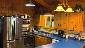 Une cuisine avec des meubles en bois, des appareils en acier inoxydable, un plan de travail bleu et un luminaire suspendu.