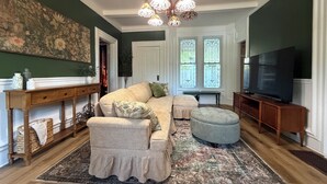 Una sala de estar con sofá, reposapiés, mesita de madera y televisor.