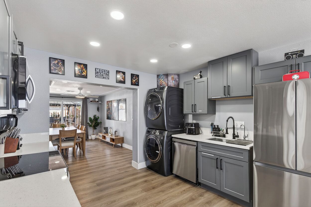 A modern kitchen with grey cabinets, a stainless steel refrigerator, a washing machine, and a dining area with a wooden table and chairs.
