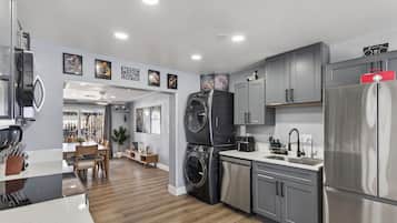 A modern kitchen with grey cabinets, a stainless steel refrigerator, a washing machine, and a dining area with a wooden table and chairs.