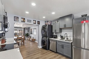Eine moderne Küche mit grauen Schränken, einem Edelstahl-Kühlschrank, einer Waschmaschine und einem Essbereich mit Holztisch und Stühlen.