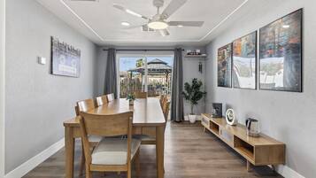 A dining area with a long wooden table, chairs, a ceiling fan, and a view of a building through a glass door.