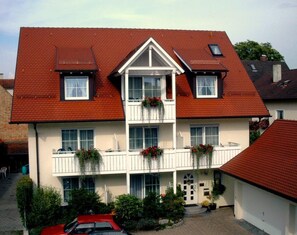 Un bâtiment à deux étages, doté d’un toit recouvert de tuiles rouges, de murs extérieurs blancs et d’un balcon central agrémenté de jardinières.