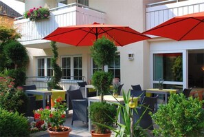 Une terrasse extérieure avec des tables et des chaises, des parasols rouges et des plantes en pot.