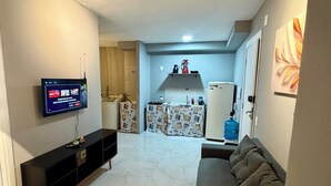A living room with a TV, sofa, and a kitchen area in the background. - Ceará Corner - Apartment on Futuro Beach (Fortaleza)