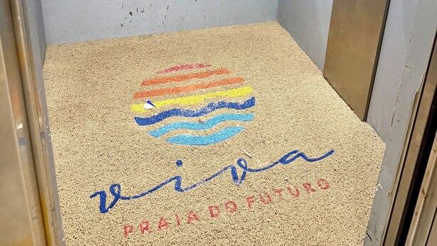 An elevator with a floor covered in colored sand art and text, a control panel with buttons, and a door with a sign indicating 'A-D'. - Ceará Corner - Apartment on Futuro Beach (Fortaleza)