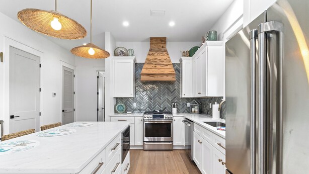 Una cocina moderna con gabinetes blancos, una isla grande, un refrigerador de acero inoxidable y un salpicadero con motivo de espiga.