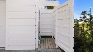 Pared exterior blanca con una puerta, un ventanal pequeño y una manguera.