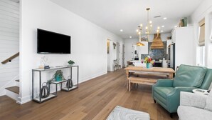 Una sala de estar moderna con un televisor de pantalla plana, un sofá de cuero verde, una mesa de comedor de madera y una cocina al fondo.