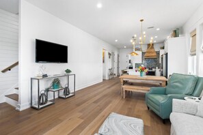 Ein modernes Wohnzimmer mit Flachbildfernseher, einem grünen Ledersofa, einem Holzesstisch und einer Küche im Hintergrund.