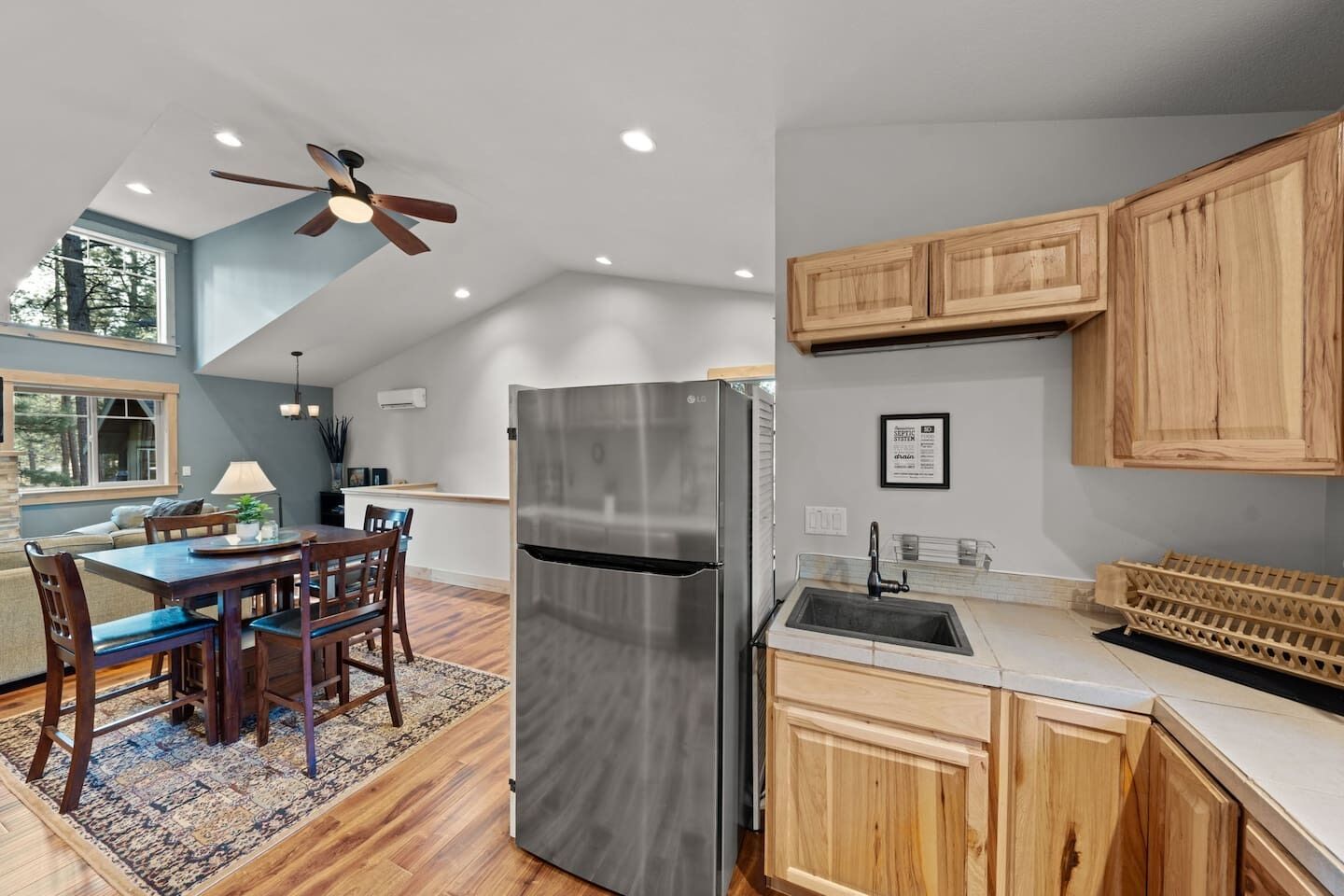 A modern kitchen with a stainless steel refrigerator, wooden cabinets, a dining area with a table and chairs, and a ceiling fan.