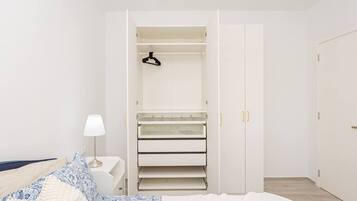 Un dormitorio con cama, una mesita de noche con lámpara, un armario con varios estantes y una puerta.
