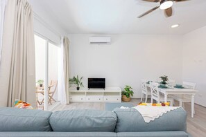 Een moderne woonkamer met een grijze bank, een flatscreen televisie, een eettafel met stoelen en een plafondventilator.