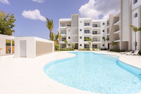 A modern hotel with a swimming pool, multiple balconies, and a clear sky.
