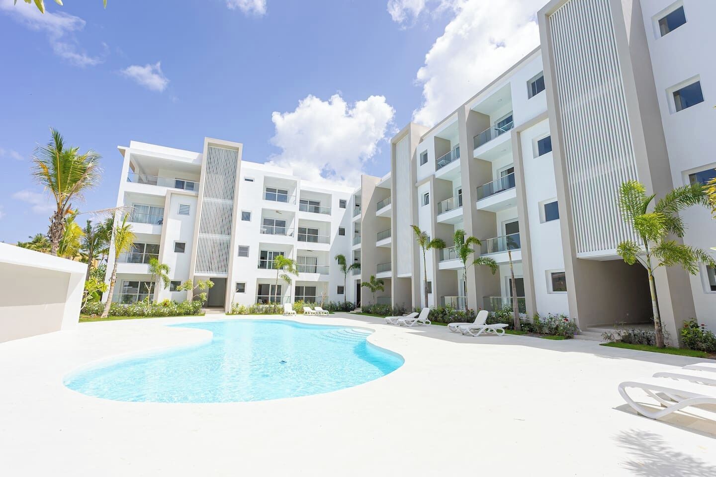 Un hotel moderno con piscina, varios balcones y palmeras.