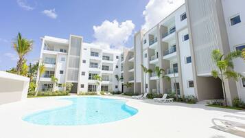 Un hotel moderno con piscina, varios balcones y palmeras.