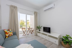 A modern living room with a sofa, TV, and a balcony with a table and chairs.