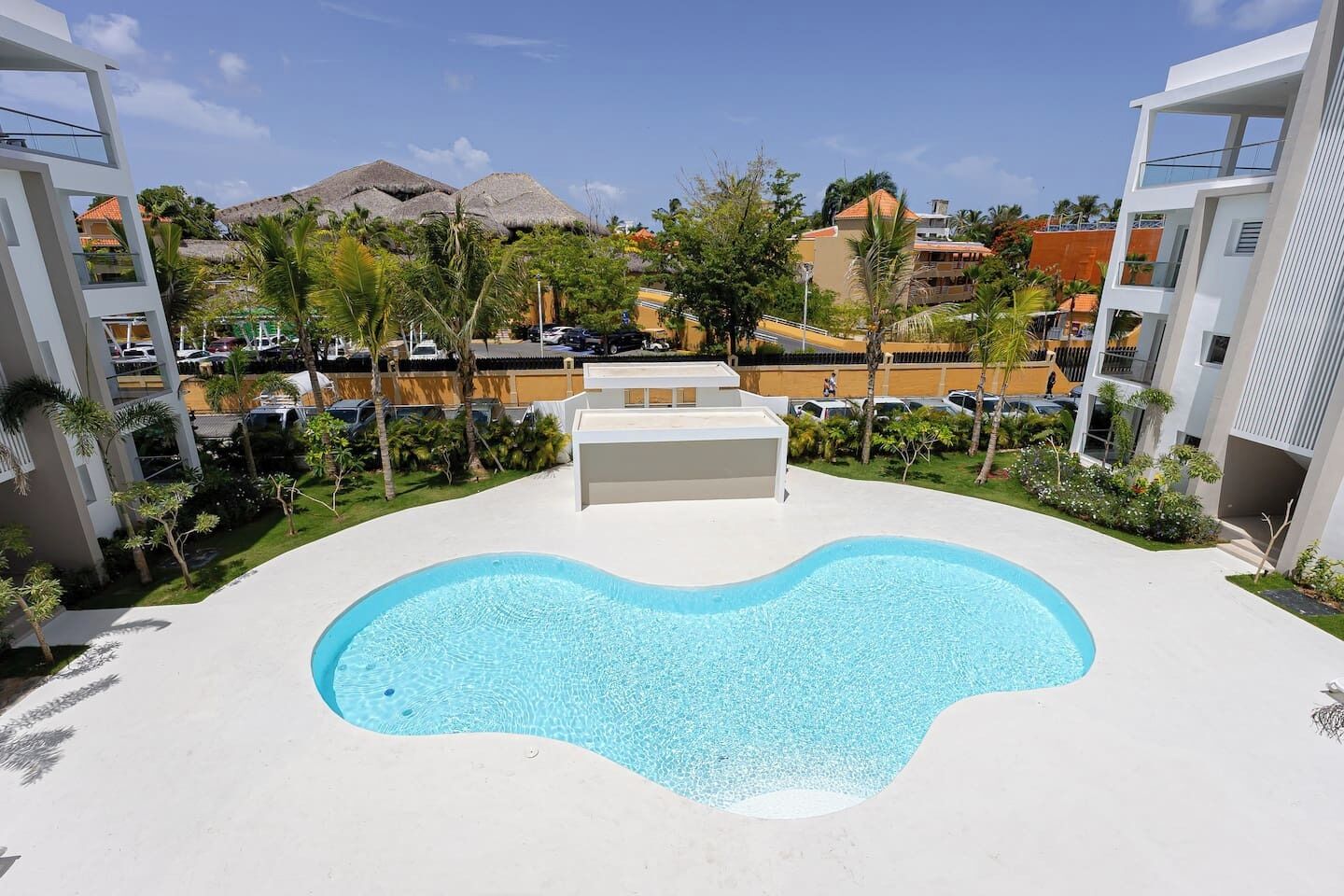 Una piscina de forma singular, rodeada de edificios modernos y palmeras.
