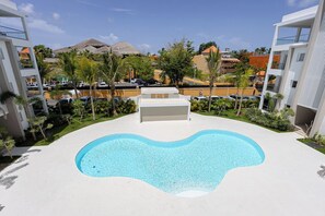 Une piscine à la forme originale, entourée de bâtiments modernes et de palmiers.