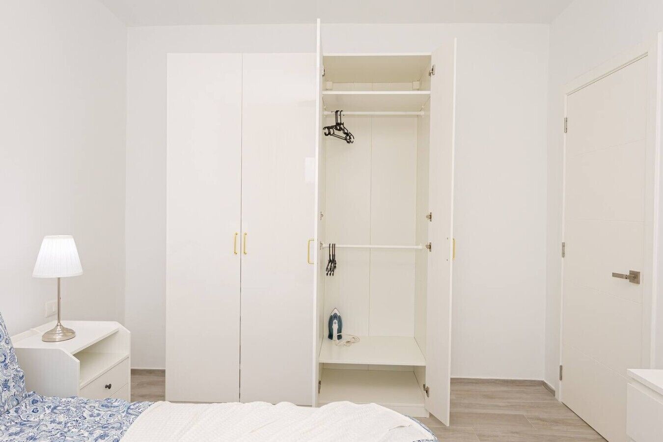 A bedroom with a bed, a nightstand, a wardrobe, and a closet with hanging items.