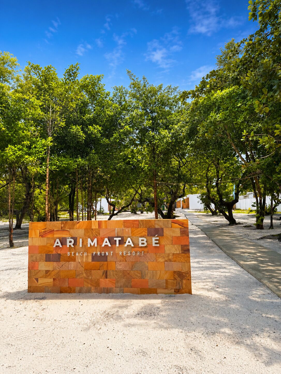 Schild für das Arimatabé Beach Front Resort mit Bäumen im Hintergrund und blauem Himmel.