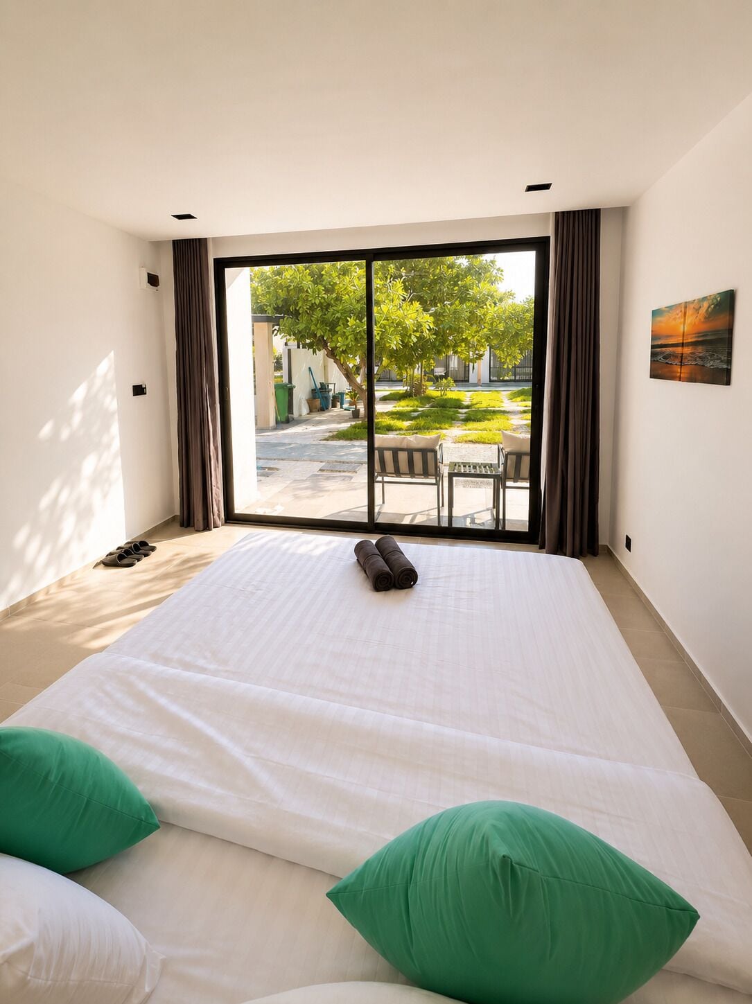A hotel room with a large bed, two green pillows, a bench outside the window, and a view of a courtyard.