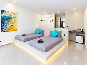 A modern hotel room with two beds, a small kitchenette, and a large painting on the wall.