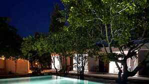A rectangular swimming pool with a light blue tint, surrounded by trees and a building with warm lighting. - ARIMATABE Beachfront Resort (Koh Rong)