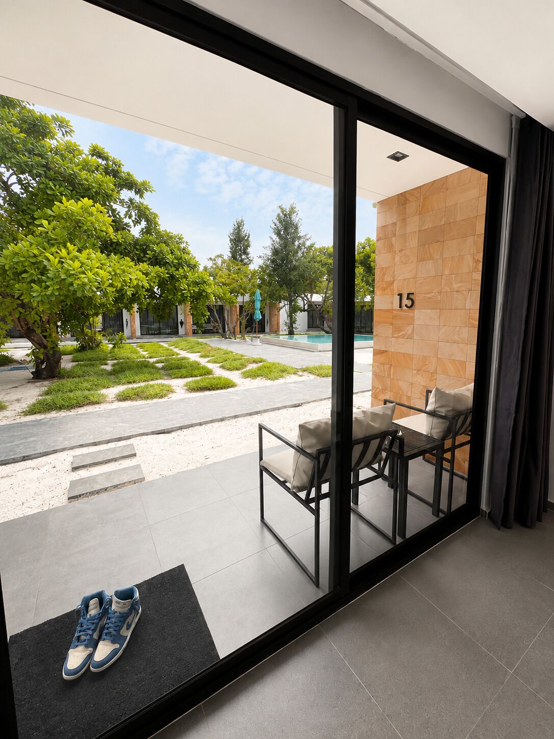 A modern hotel room with a glass door leading to a pool area, a number '15' on the wall, and a pair of shoes on the floor.