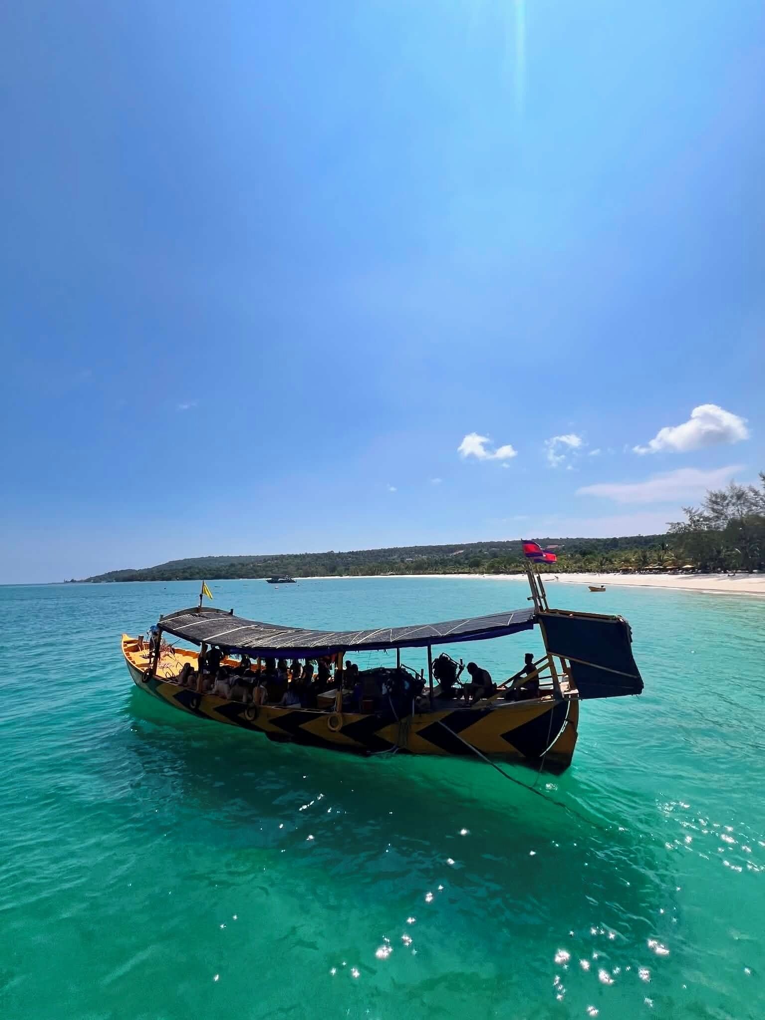 A boat with a canopy and passengers, floating on clear turquoise water.