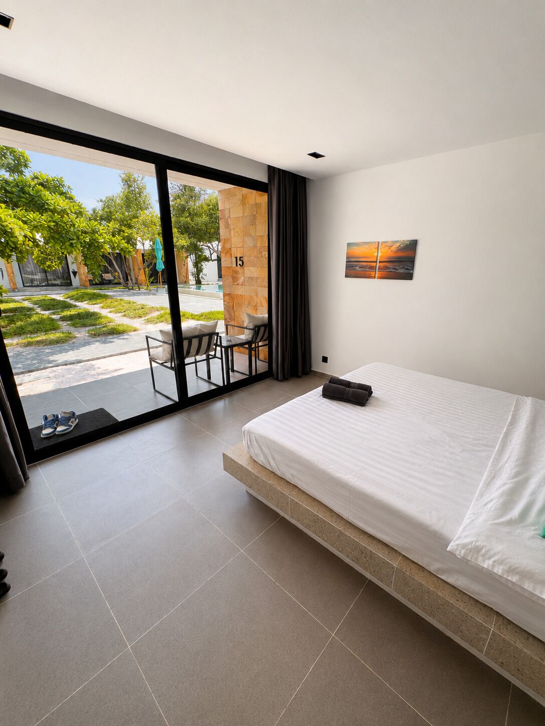 Habitación de hotel moderna con un amplio ventanal corredera que da a un espacio exterior con piscina y vegetación.