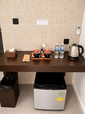 A hotel room with a wooden table, a trash bin, a refrigerator, and a sign indicating wifi availability.