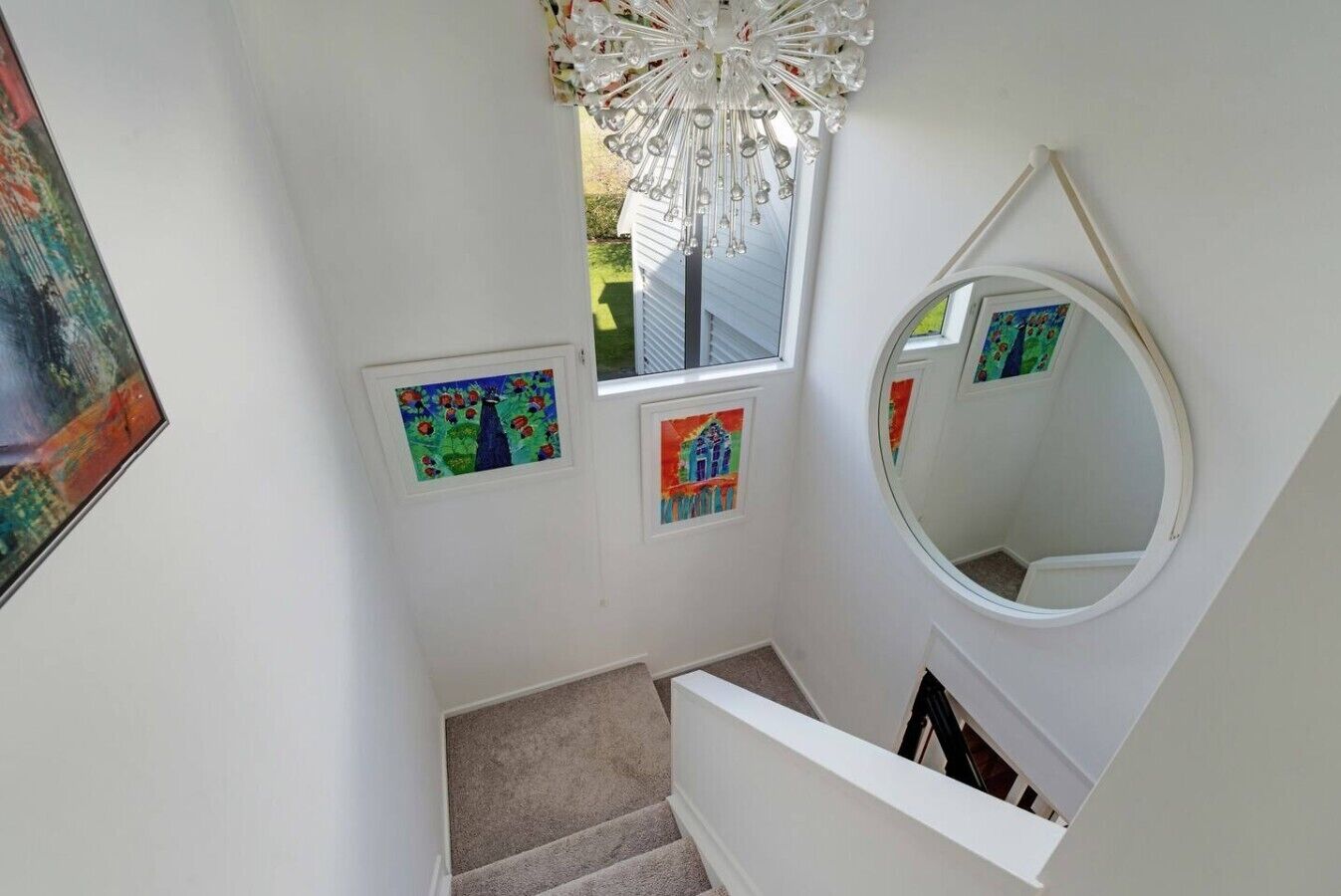 A staircase with a round mirror, a chandelier, and three framed artworks.