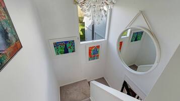 A staircase with a round mirror, a chandelier, and three framed artworks.