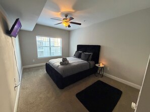A bedroom with a bed, a ceiling fan, a window, and a small bedside table with a candle. - Diamond Key Retreats!!Your Favorite Modern Getaway (Atlanta)