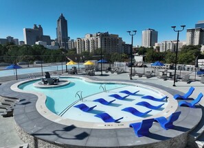Ein Pool mit blauen Liegestühlen, einer Springbrunnen und einer Stadtkulisse im Hintergrund.