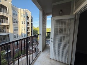 Ein Balkon mit Blick auf benachbarte Gebäude, eine Tür mit Rollläden und eine kleine Außenfläche mit einem Blumentopf.