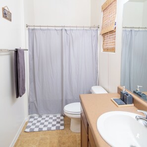Ein Badezimmer mit Duschvorhang, Toilette, einer karierten Matte, Waschbecken und Spiegel.