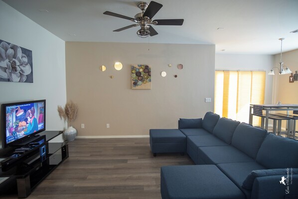 A living room with a sectional sofa, a flat-screen TV, a ceiling fan, and artwork on the walls. - Sierra Vista Hideaway / 5 minutes to Fort Huachuca (Sierra Vista)