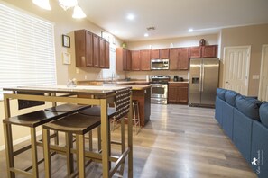 A modern kitchen with wooden cabinets, stainless steel appliances, and a bar area with stools.